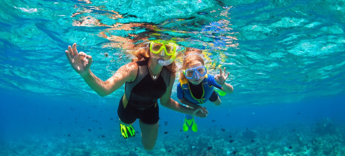 Mutter und Kind mit Schnorchelmaske tauchen unter Wasser mit tropischen Fischen im Korallenriff-Meeresbecken.