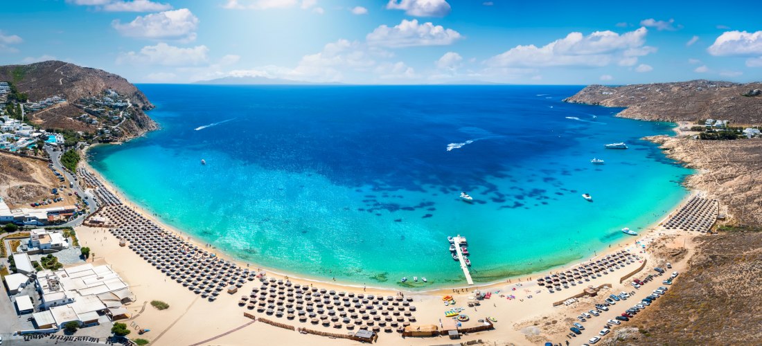 Panoramablick auf den Paradise Beach auf Mykonos mit türkisfarbenem Wasser, Strandliegen und Booten in der Bucht