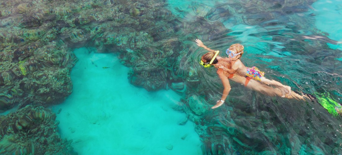 Mutter und Kind mit Schnorchelmaske tauchen unter Wasser und erkunden tropische Fische im Meeresbecken des Korallenriffs.
