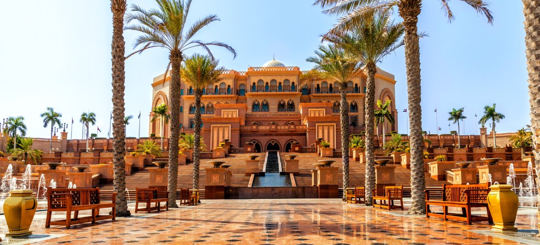 Prunkvolle Fassade des Emirates Palace in Abu Dhabi mit Palmen, Wasserfontänen und einer prachtvollen Eingangstreppe