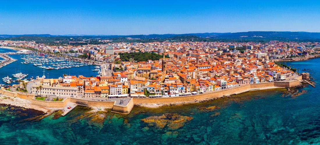 Panoramablick auf Alghero auf Sardinien mit Altstadt, Stadtmauer und Hafen im türkisblauen Mittelmeer – Sehenswürdigkeit an der Nordwestküste der Insel
