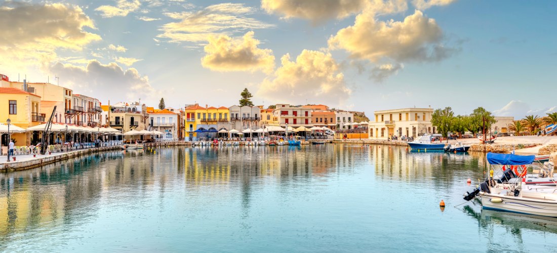 Venezianischer Hafen von Rethymno auf Kreta bei Sonnenuntergang mit bunten Häusern, Restaurants am Wasser und kleinen Booten im ruhigen Hafenbecken