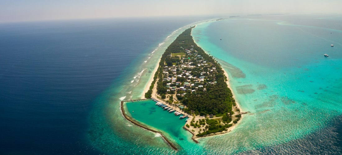 Luftaufnahme einer schmalen bewohnten Insel der Malediven mit Hafen, Häusern und türkisfarbenem Wasser