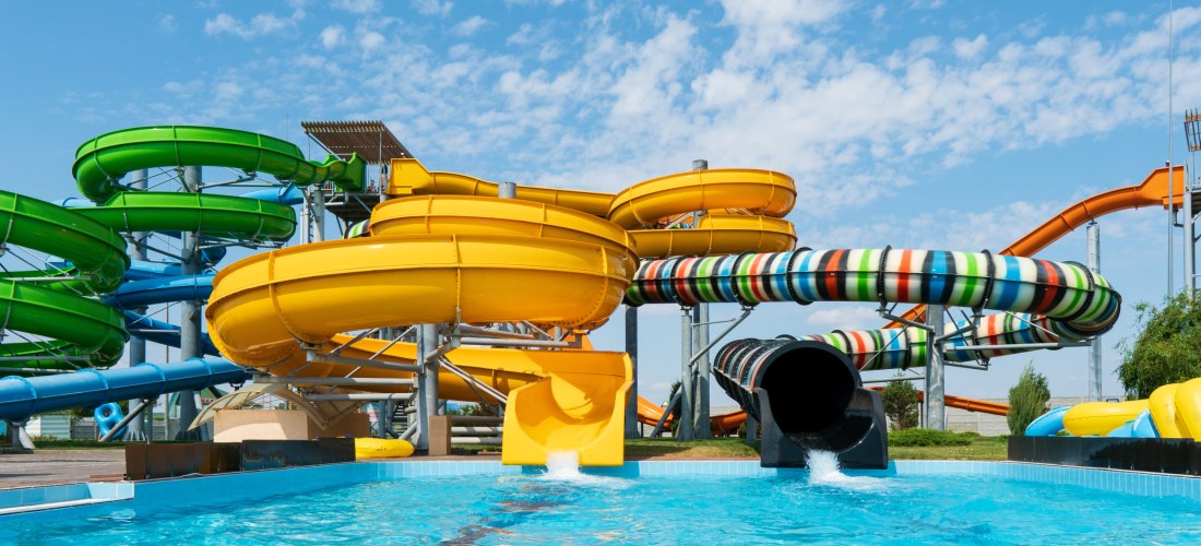 Mehrere bunte Wasserrutschen führen in ein Schwimmbecken unter blauem Himmel in einem modernen Wasserpark