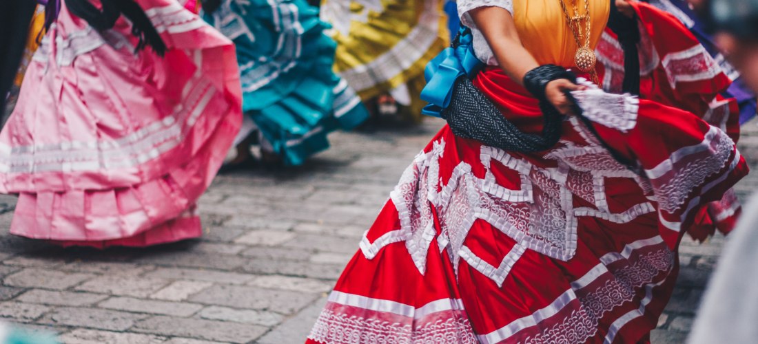 Gruppe von Tänzerinnen in traditionellen, bunten mexikanischen Kleidern mit Rüschen und Spitze, die während einer folkloristischen Tanzaufführung schwungvoll ihre Röcke schwingen