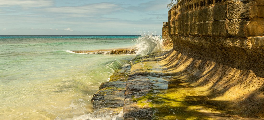 Karibisches Meer mit türkisblauem Wasser, das gegen eine alte Ufermauer auf Barbados schlägt.