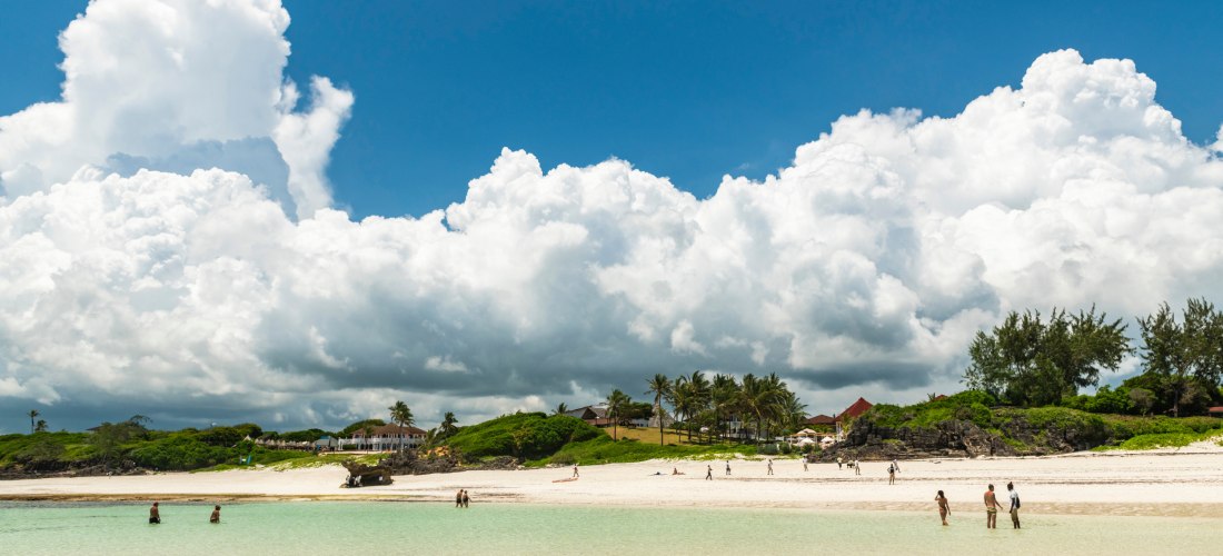 Badegäste am weißen Sandstrand von Watamu Beach, Kenia – Palmen, türkisblaues Wasser und tropische Kulisse.