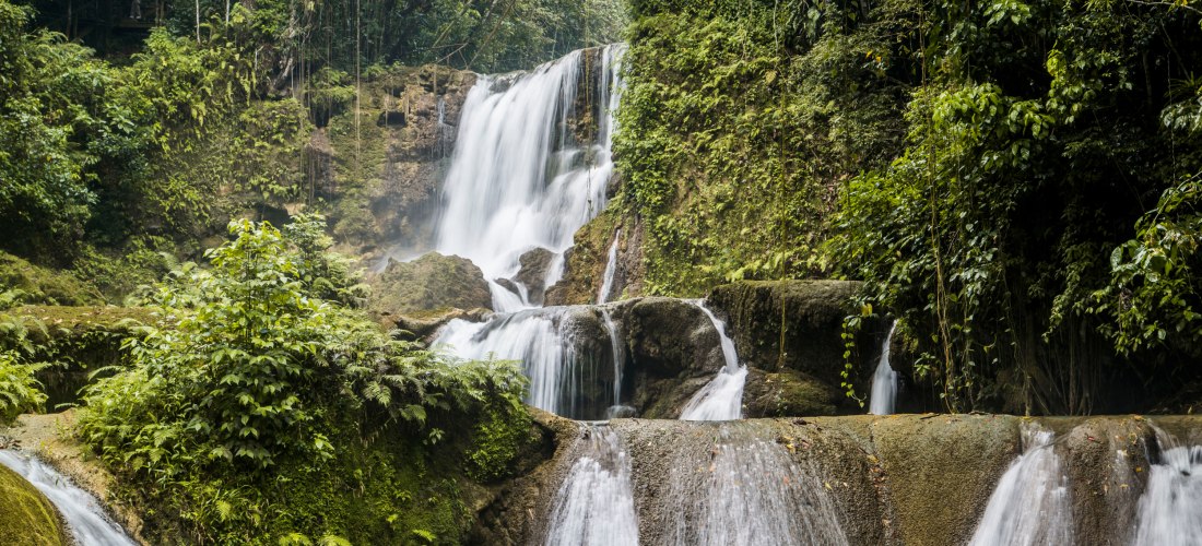 Mehrstufiger Wasserfall im tropischen Regenwald – üppige Vegetation und moosbewachsene Felsen umgeben das herabstürzende Wasser.