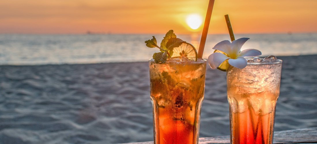 Zwei erfrischende Cocktails mit Minze und Zitrone auf einem Holztisch am Strand bei Sonnenuntergang