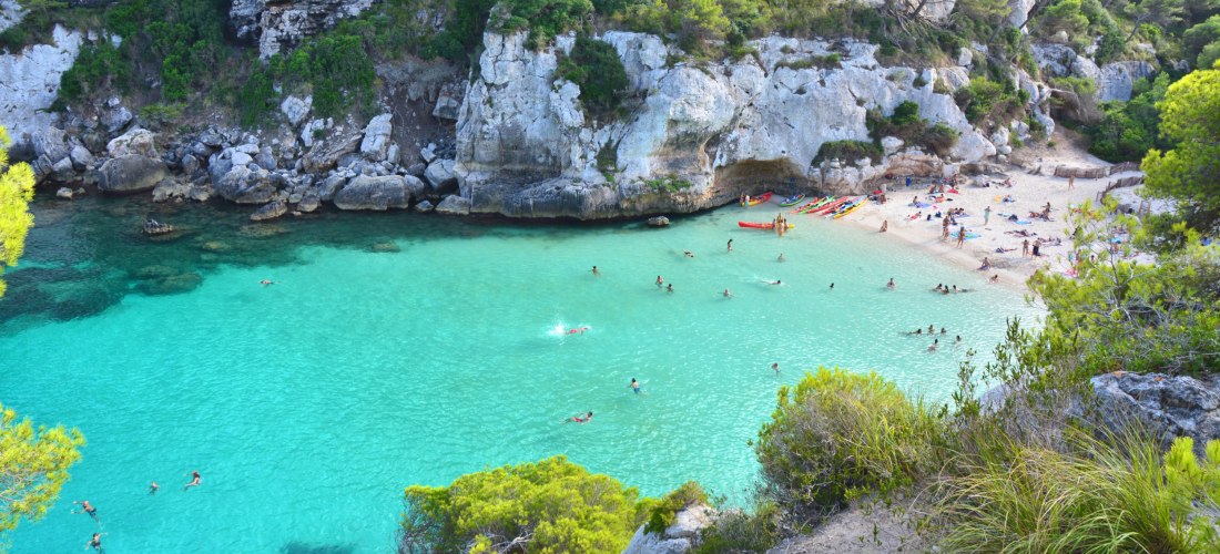 Cala Macarella auf Menorca: idyllische Bucht mit feinem Sandstrand, türkisblauem Wasser und umgeben von steilen Felsen und Pinienwäldern.