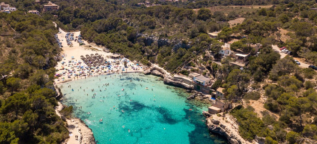 Luftaufnahme des Strandes Cala Llombards auf Mallorca mit türkisblauem Wasser, Badegästen und umliegender mediterraner Natur