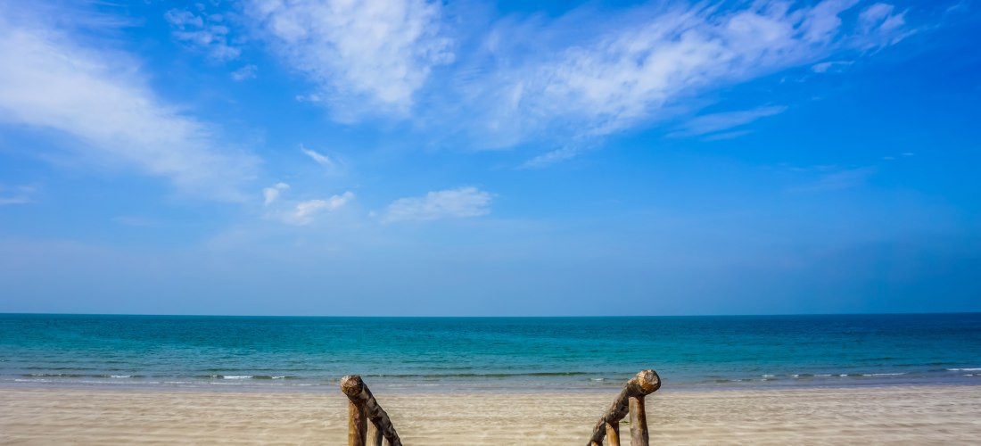 Holztreppe führt zu einem ruhigen Sandstrand mit türkisblauem Meer und klarem Himmel