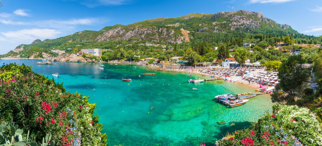 Paleokastritsa auf Korfu – idyllische Bucht mit türkisblauem Meer, Strand und grünen Hügeln im Hintergrund