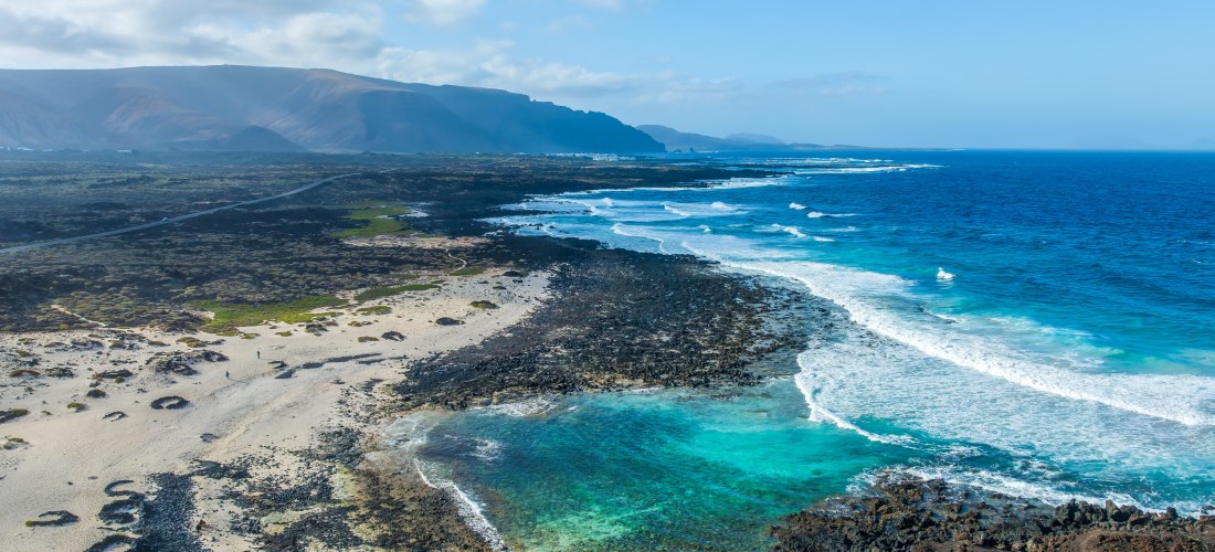 Luftaufnahme der Küste bei Orzola auf Lanzarote mit schwarzem Lavagestein, hellem Sandstrand und türkisblauem Atlantik.