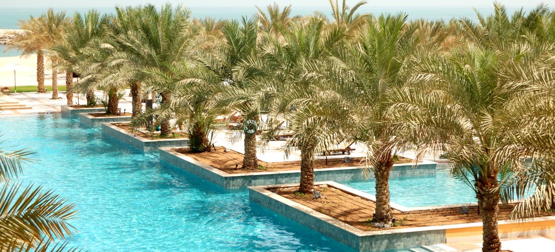 Luxuriöser Pool mit Palmeninseln, klarem Wasser und Blick auf das Meer