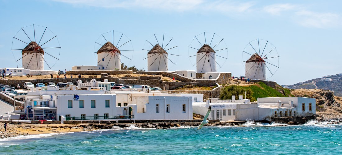 Panoramablick auf die Windmühlen von Kato Mili oberhalb der weißen Häuser von Mykonos-Stadt am Meer