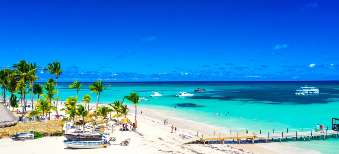 Karibikstrand in Punta Cana mit Palmen, Booten, Steg und türkisfarbenem Wasser in der Dominikanischen Republik