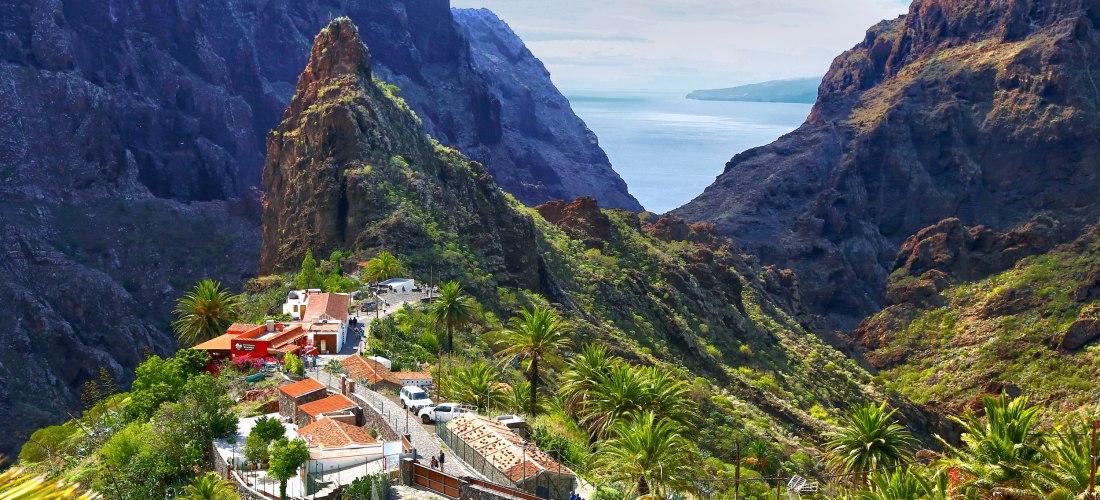 Blick auf das Bergdorf Masca auf Teneriffa mit Palmen, Felsen und Meer im Hintergrund