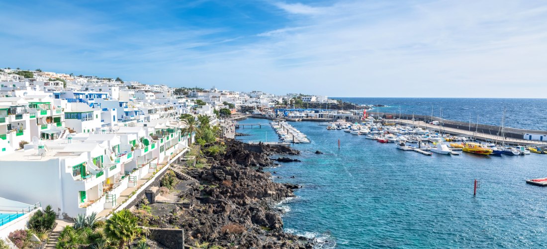 Blick auf den Hafen von Puerto del Carmen auf Lanzarote mit weißen Häusern, Yachten und türkisblauem Meer.