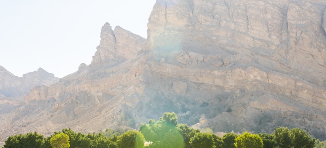 Beeindruckende Felsformationen der Hajar-Berge in Fujairah, Vereinigte Arabische Emirate. Karge Berglandschaft mit grüner Oase im Vordergrund – beliebtes Ziel für Naturfreunde.