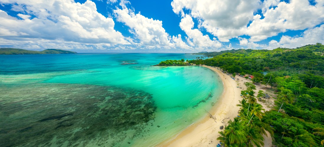 Bogenförmige Bucht mit türkisblauem Meer, hellem Sandstrand und Palmen in der Dominikanischen Republik – tropische Küstenlandschaft