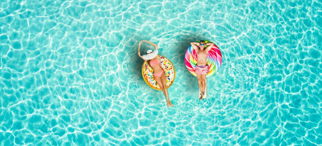 Ein Paar genießt die Sonne auf farbenfrohen Schwimmreifen im türkisblauen Wasser. Die perfekte Szene für pure Entspannung und sommerliche Urlaubsstimmung.