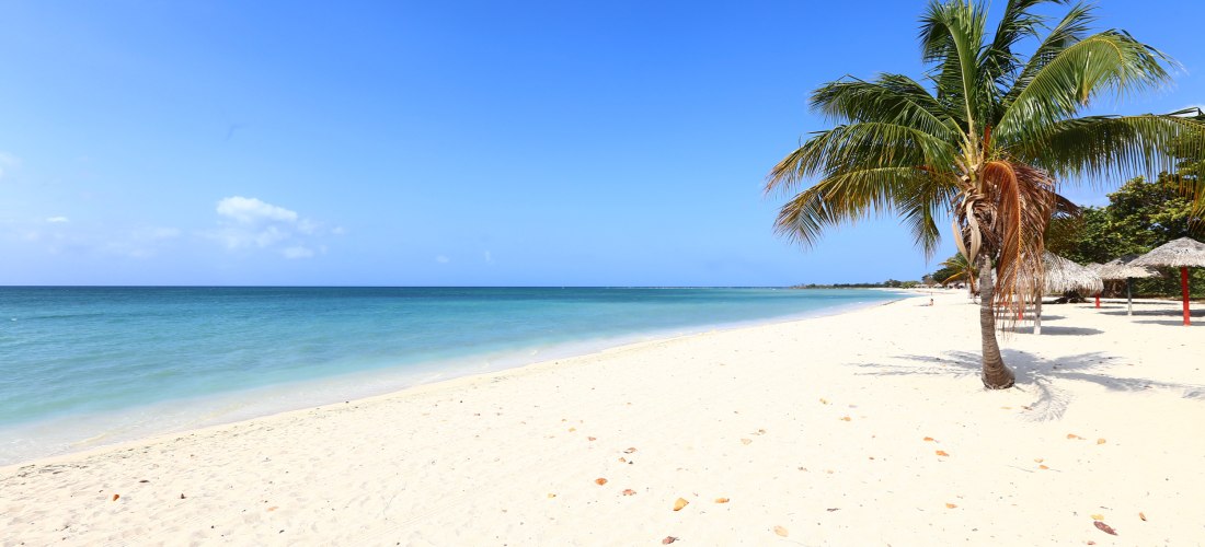 Playa Ancón – Traumstrand mit türkisblauem Meer und Palmen Idyllischer Strand an der Playa Ancón bei Trinidad auf Kuba mit feinem weißen Sand, türkisblauem Meer, Palmen und Strohdächern unter strahlend blauem Himmel.
