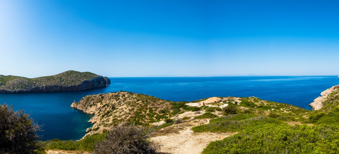 Panoramablick auf eine zerklüftete Küste mit grün bewachsenen Hügeln und tiefblauem Meer unter klarem, blauem Himmel