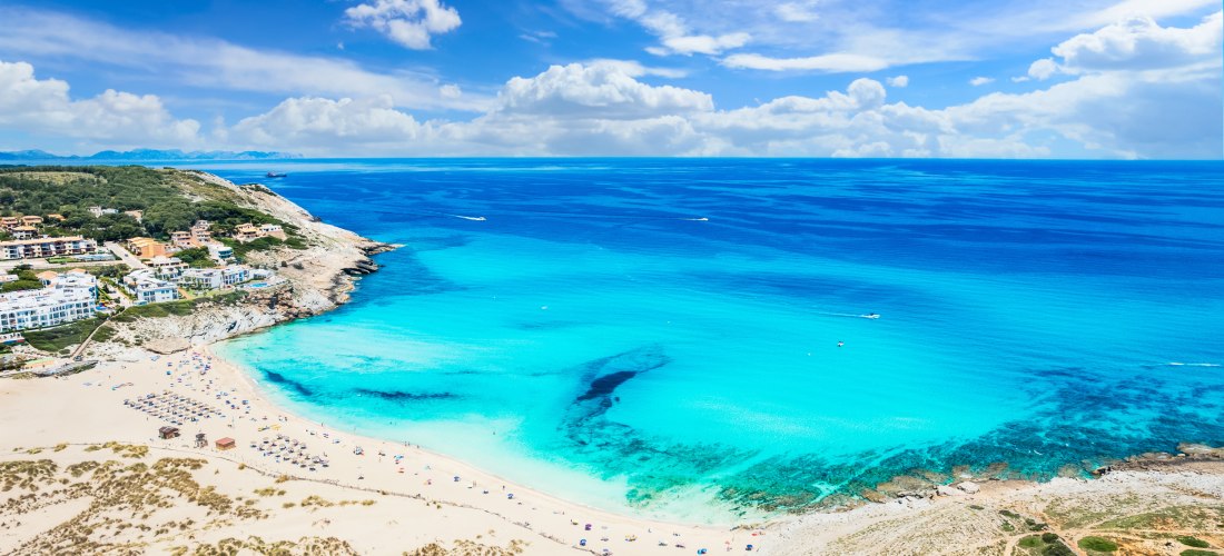 Luftaufnahme der Cala Mesquida auf Mallorca mit weißem Sandstrand, türkisblauem Meer und Ferienhäusern am Hang