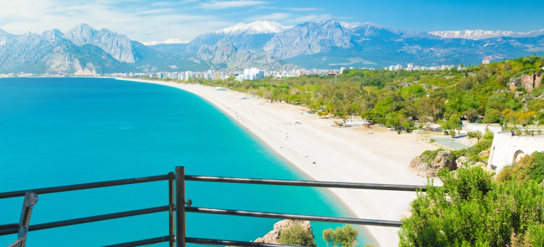 Konyaaltı-Strand in Antalya, Türkei: ruhiges türkisfarbenes Mittelmeer, blauer Himmel und üppiges Grün. 