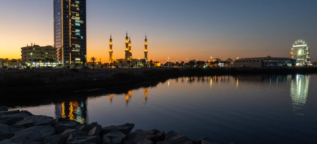 Skyline von Ras Al Khaimah bei Sonnenuntergang mit Moschee, Riesenrad und Wasserreflexionen an der Corniche.