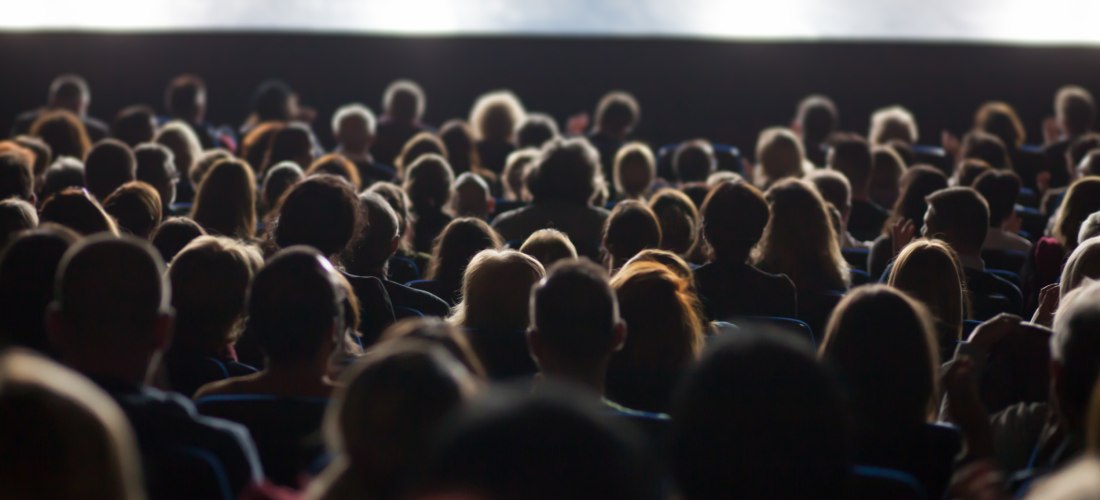 Publikum im Kino, Leiwand im Hintergrund und im Vordergrund viele Gäste, unscharf