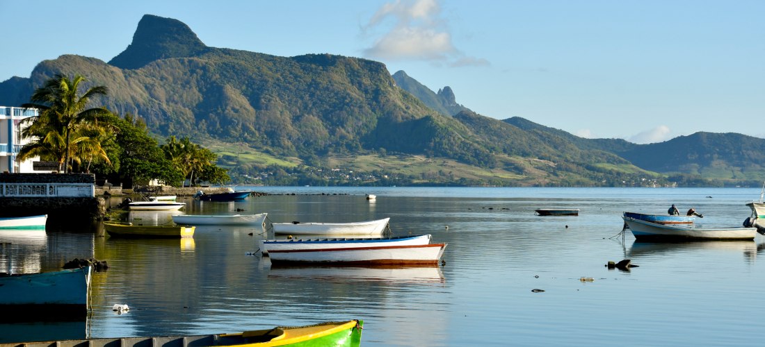 Bunte Fischerboote im ruhigen Wasser der Bucht von Mahébourg mit Blick auf die grünen Berge von Mauritius