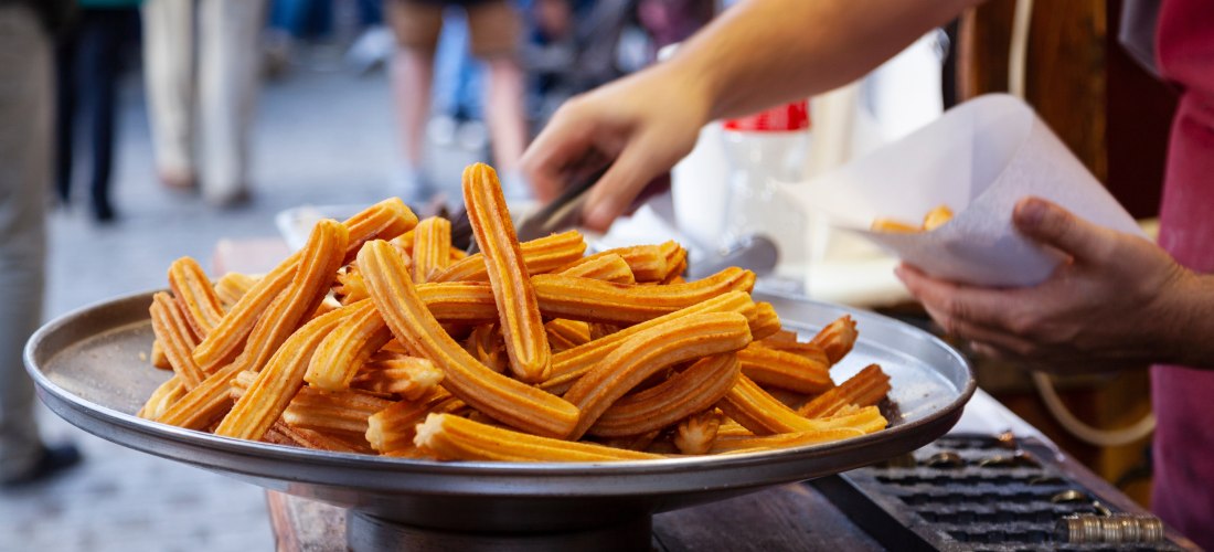 Frische Churros auf einem großen Tablett, während ein Verkäufer sie in eine Tüte verpackt