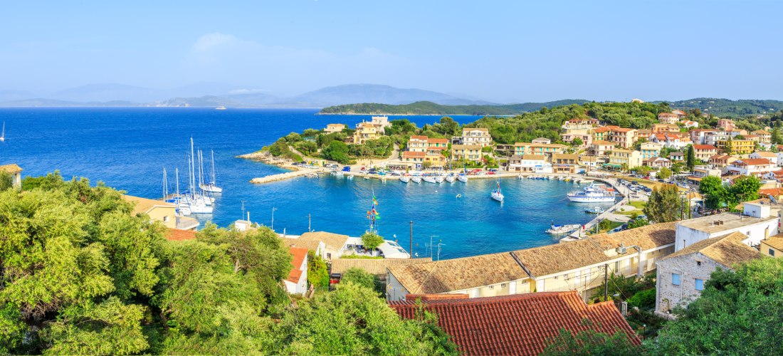 Panoramablick auf die Bucht von Kassiopi mit Segelbooten und bunten Häusern am Wasser