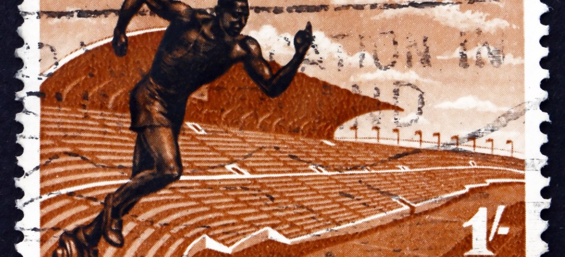 Jamaikanische Briefmarke mit der Aufschrift 'National Stadium' und 'Jamaica' in Großbuchstaben. Abgebildet ist ein stilisierter Sprinter in dunkler Farbe, der aus den Zuschauerreihen eines großen Stadions auf eine Laufbahn sprintet. Der Hintergrund ist in