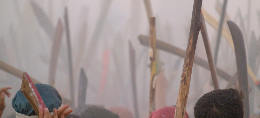 Nahaufnahme von Menschen mit erhobenen Holzstöcken in einer dichten Rauchwolke, aufgenommen während des Festes 'Moros i Cristians' in Sóller. Viele Teilnehmer tragen Kopfbedeckungen oder bunte Kleidung. Die Szene wirkt intensiv und emotional – symbolträch