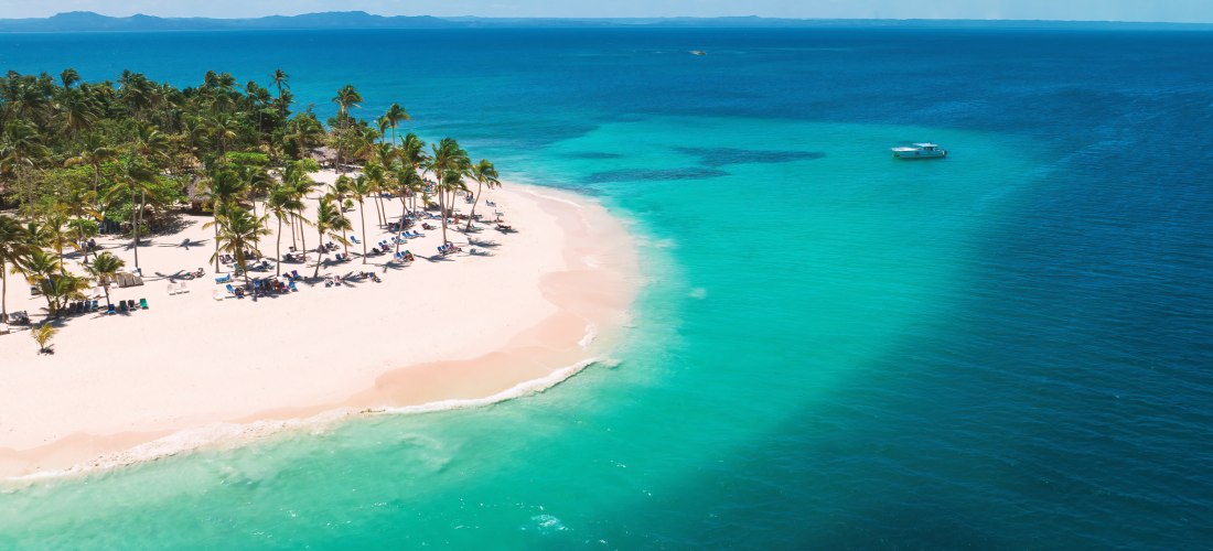 Traumstrand der Dominikanischen Republik mit weißem Sand, Palmen und türkisfarbenem Wasser – ein Boot liegt vor der Küste.
