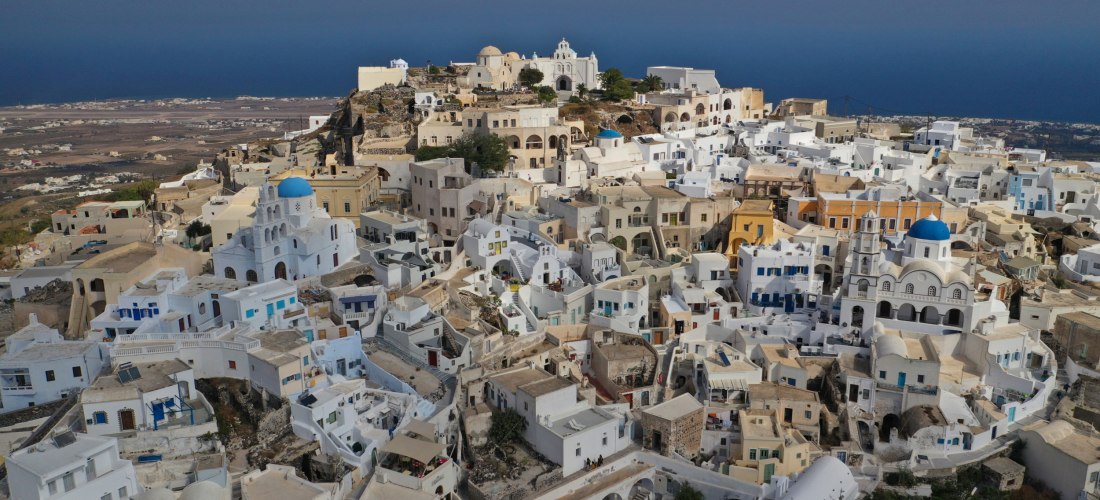 Panoramablick auf Pyrgos, Santorini: verwinkelte Gassen, weiße Häuser und Kirchen mit blauen Kuppeln hoch über der Insel