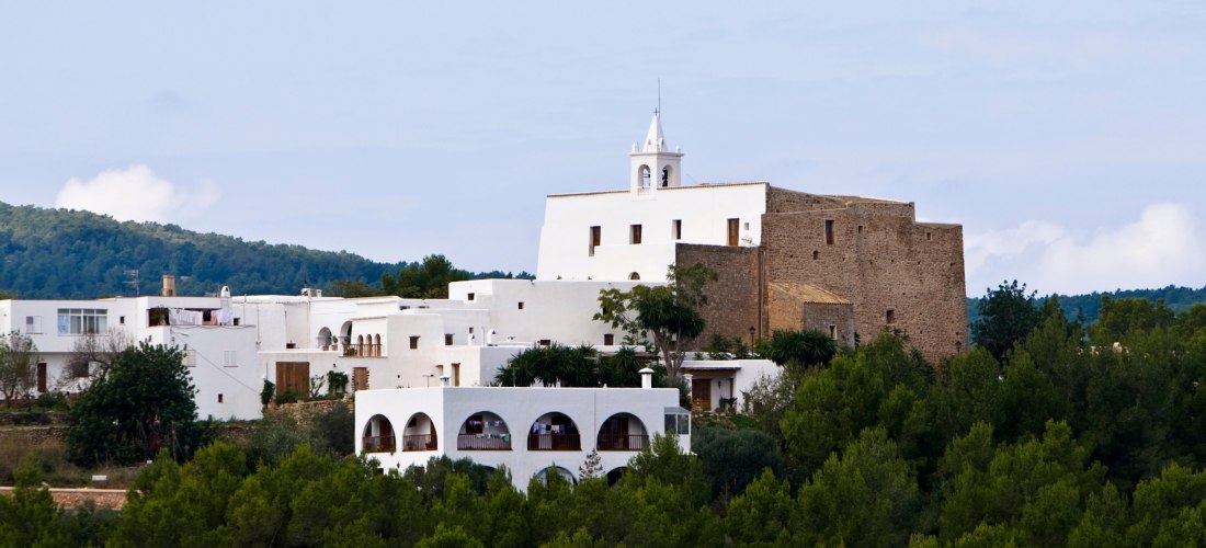 Blick auf das Dorf Sant Josep de sa Talaia auf Ibiza mit weiß getünchten Häusern und der traditionellen Kirche, die sich über den grünen Kiefernwald erhebt.