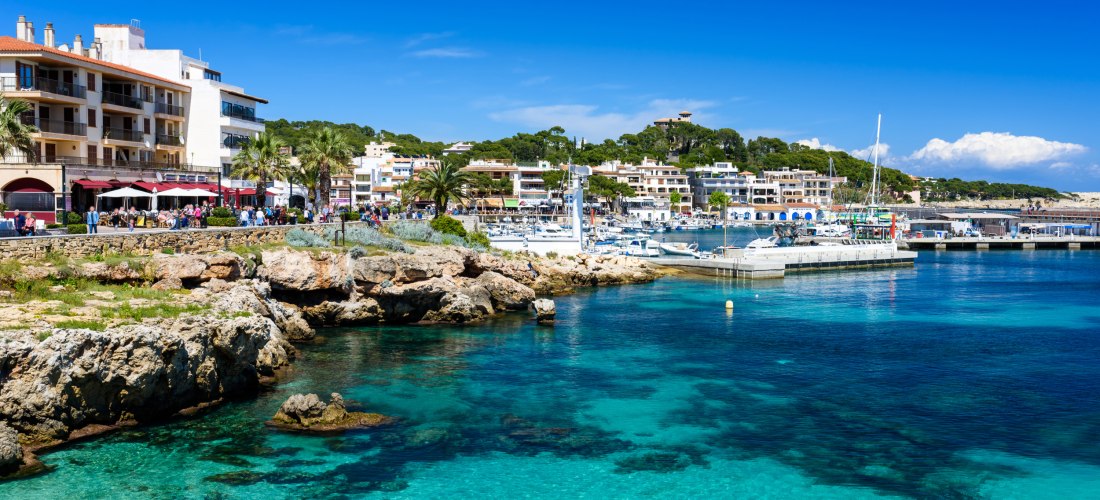 Hafen von Cala Ratjada mit Promenade, Cafés und kristallklarem Wasser – perfektes Reiseziel für Paare auf Mallorca