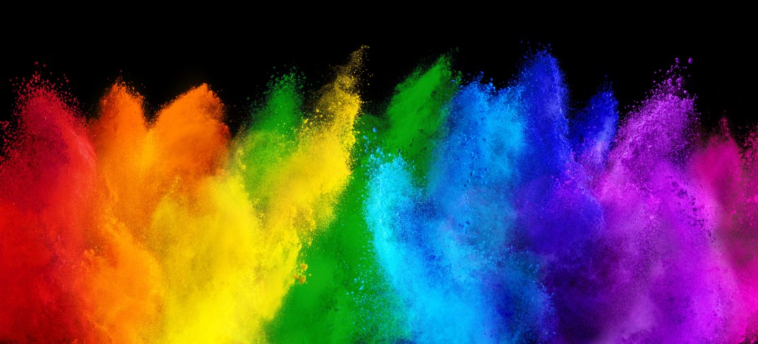 Explosion von buntem Farbpulver auf schwarzem Hintergrund. Die Farben verlaufen von links nach rechts in Regenbogenabfolge: Rot, Orange, Gelb, Grün, Blau, Violett und Pink. Die Pulverwolken wirken dynamisch und kraftvoll