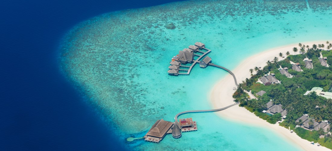 Exklusive Overwater-Villen auf den Malediven, verbunden durch Stege mit einer luxuriösen Resort-Insel mit Palmenstrand und türkisfarbenem Wasser.