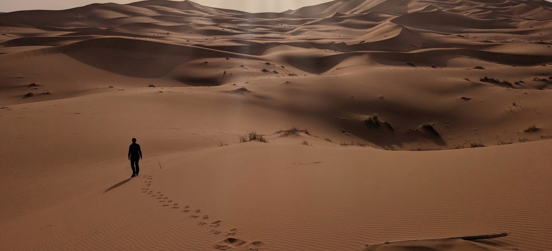 Person wandert durch die goldenen Sanddünen des Erg Chebbi in der Sahara bei Merzouga, Marokko – spektakuläre Wüstenlandschaft bei Sonnenlicht.