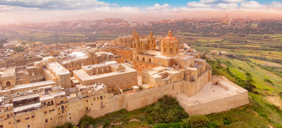 Luftaufnahme der ummauerten Altstadt Mdina auf Malta mit Kathedrale, historischen Gebäuden und grüner Landschaft im Hintergrund