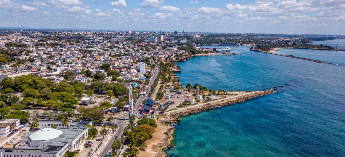 Luftaufnahme einer Küstenstadt mit Promenade, türkisblauem Meer und Hafen – Uferstraße mit Palmen