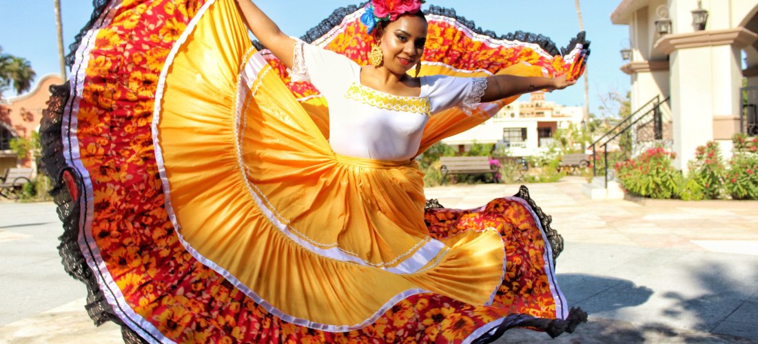 Mexikanische Tänzerin in einem bunten, traditionellen Kleid mit gelben und roten Farbtönen führt einen folkloristischen Tanz auf, während sie das Kleid schwungvoll bewegt