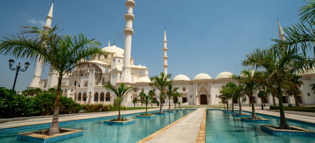 Scheich-Zayid-Moschee in Fujairah mit Palmenallee und Wasserbecken. Prunkvolle weiße Fassade, Kuppeln und Minarette – eines der Highlights der Emirate.