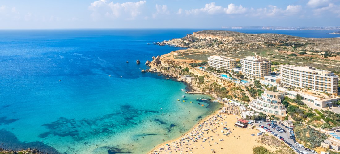 Golden Bay auf Malta mit hellem Sandstrand, türkisfarbenem Meer und Hotels oberhalb der Bucht aus der Vogelperspektive