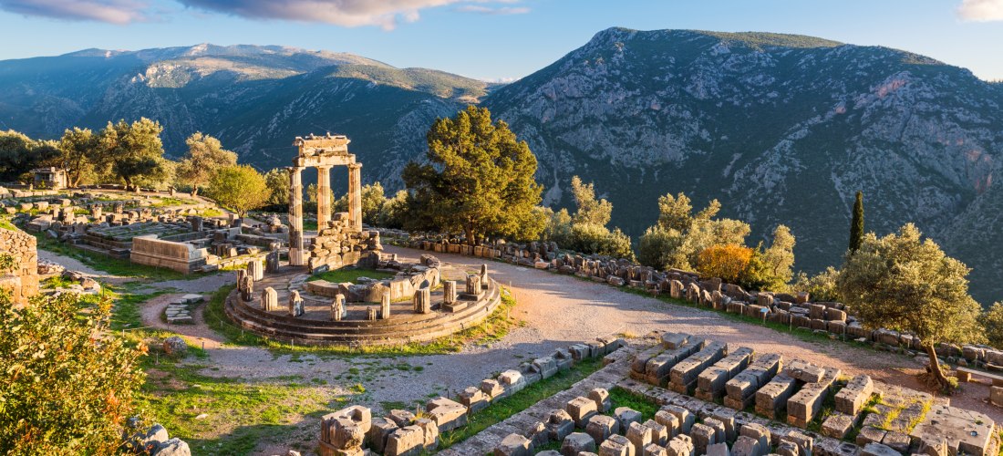 Ruinen des Tholos von Delphi in Griechenland, umgeben von Bergen und grüner Landschaft